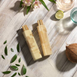 Guava and gold shampoo and conditioner on wooden deck, leaves, coconut, lime, water and flowers