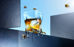 Melting whisky tumbler with honey bees on grey ledge with sunny sky background