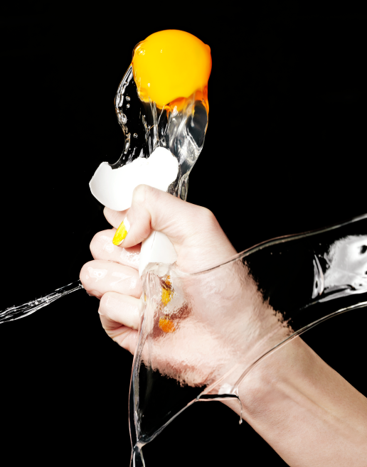Female model hand with white and yellow two-tone manicure crushing an egg making it pop.